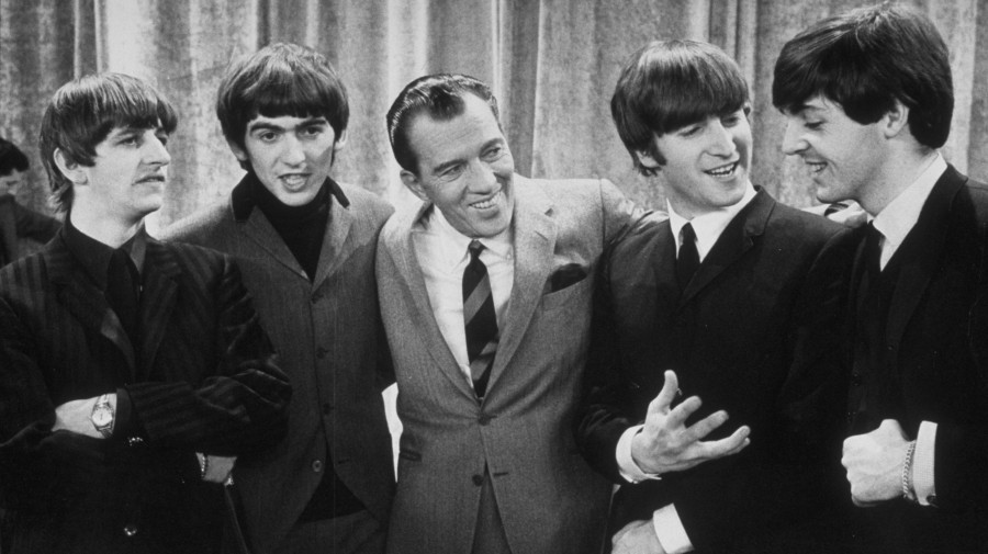 Ed Sullivan (center) smiles while standing with The Beatles on the set of his variety show on February 9, 1964.