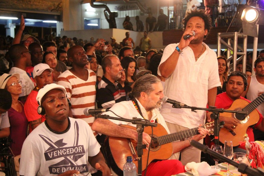 Sitting around what looks like a conference table with a small group of musicians, guitarist Moacyr Luz (center) leads his samba group.